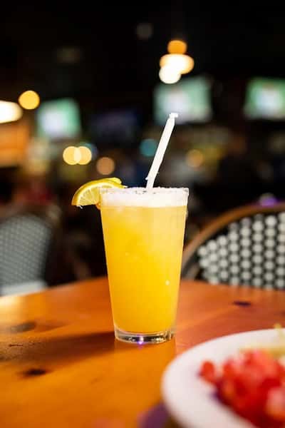 Bright orange cocktail garnished with a lemon wedge and salt rim, served in a tall glass with a straw on a wooden table.