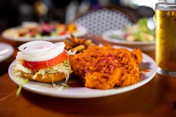Crispy fried chicken sandwich with lettuce, tomato, and onion served with fries and a cold beer on a wooden table.