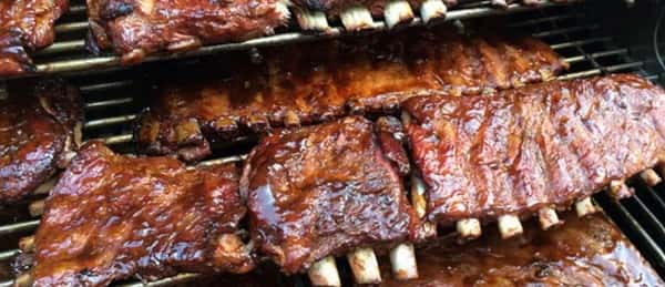 Glazed barbecue ribs stacked on a grill, coated in a rich, smoky sauce with a caramelized finish.