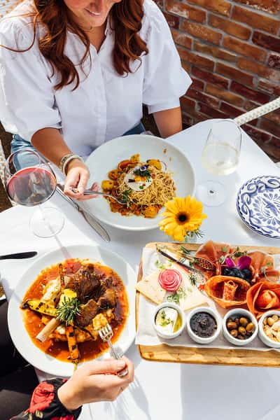 Person seated at a table with a plate of pasta, charcuterie board and entree