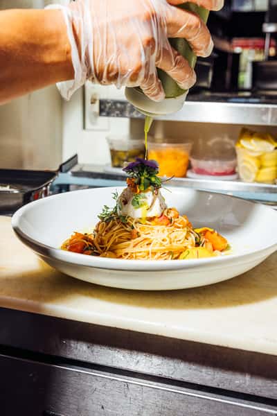 Sauce being drizzled on top of a plate of pasta
