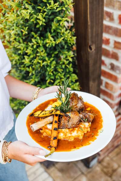 Person holding a plate of food with meat, mashed potatoes and roasted veggies