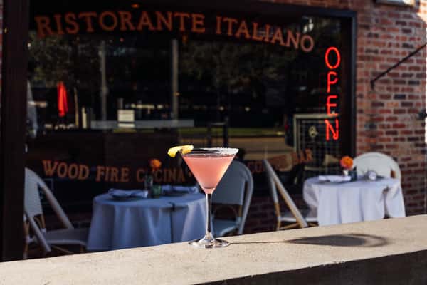 Pink cocktail topped with a citrus peel on a countertop in front of Enoteca Rossa
