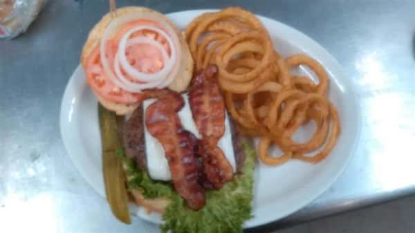 burger on a roll with lettuce, tomatoes, onions, and bacon with a side of onion rings
