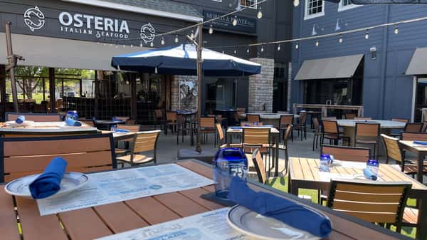Place settings on the patio at Osteria, with signature blue napkins, menus, and glassware—ready for brunch, lunch, or dinner in Westport Village