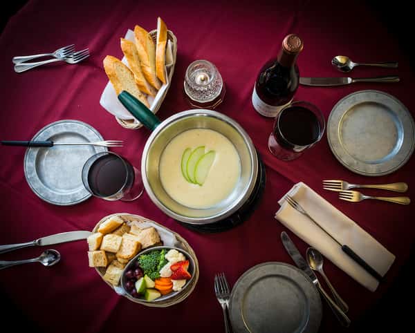 Overhead view of a table with a fondue pot, veggies, bread, and wine
