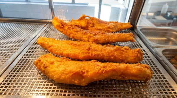 Large golden battered fish fillets freshly cooked and displayed on a draining rack.