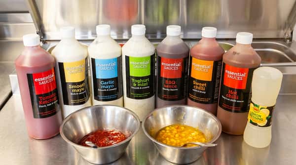 Selection of colourful takeaway sauces in bottles with dipping sauces prepared in metal bowls.