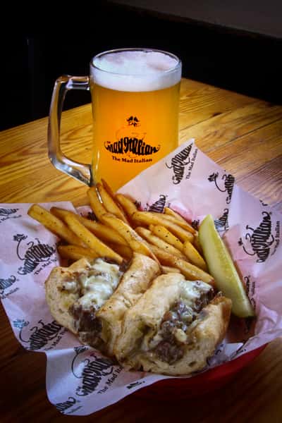 Cheesesteak with crispy fries, pickle wedge and a cold beer