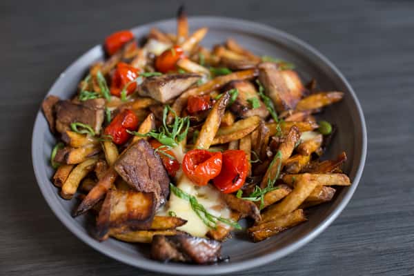 This image features a vibrant stir-fry dish loaded with bold colors and textures. Tender slices of beef are tossed with crispy golden fries, sautéed onions, and bright red bell peppers, all coated in a glossy, savory sauce. Fresh herbs add a touch of green, enhancing both the flavor and presentation. The combination of hearty meat, crispy potatoes, and vegetables creates a rich and satisfying dish with a modern, flavorful twist.