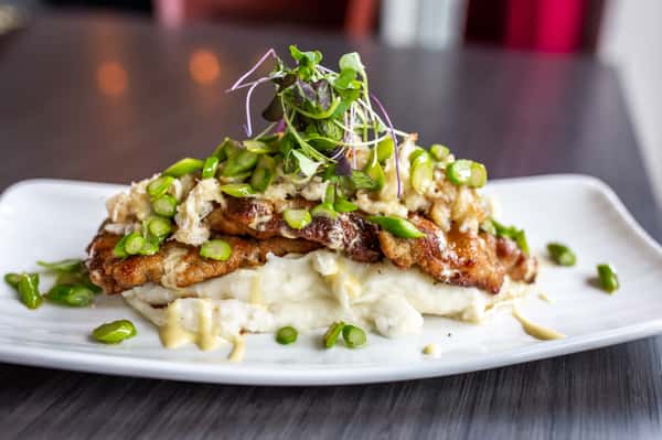 This dish showcases a beautifully seared piece of fish, likely salmon, glazed with a rich sauce and topped with chopped nuts and fresh herbs. It rests on a bed of creamy grains or risotto, creating a balance of texture and flavor with a refined presentation.