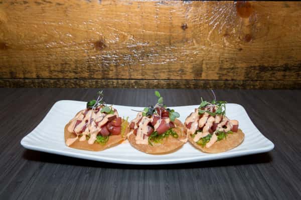 This dish features elegant bite-sized crostinis topped with finely diced meat or fish, garnished with herbs and a drizzle of sauce. Beautifully plated, it's a refined appetizer perfect for sharing.