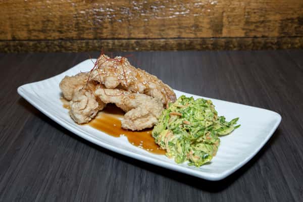 A beautifully plated seafood dish, likely crab cakes or stuffed seafood, is finished with a light glaze and sprinkled with sesame seeds. It's paired with a fresh, finely chopped slaw, adding crunch and contrast.