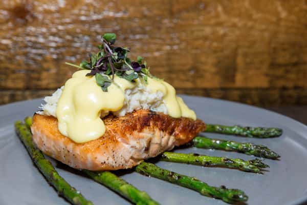 A perfectly seared salmon fillet is topped with a creamy, rich sauce and served over a bed of tender asparagus. Finished with fresh microgreens, the dish is both elegant and full of flavor.