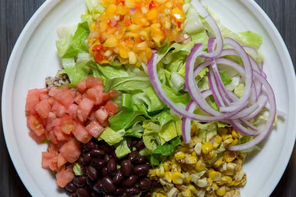A vibrant, fresh salad bowl filled with crisp lettuce, black beans, corn, diced tomatoes, red onions, and colorful peppers. The mix of textures and bright ingredients makes it both healthy and visually appealing.
