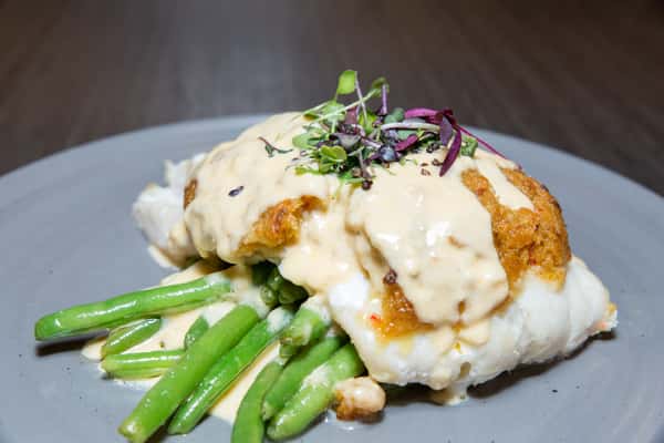 A comforting entrée featuring crispy chicken topped with a rich, creamy sauce, served alongside tender green beans. The dish is finished with a touch of herbs, creating a warm and satisfying presentation.