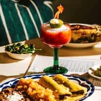 Mexican entrée with enchiladas, rice and beans, paired with vibrant layered cocktail on restaurant table