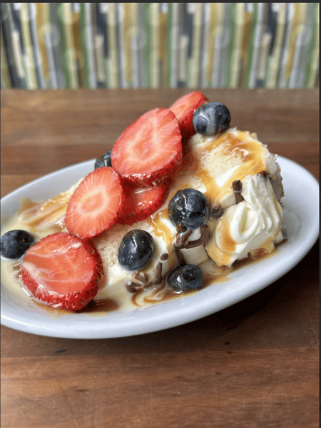 Slice of cheesecake topped with strawberries, blueberries, caramel drizzle, and whipped cream on white plate