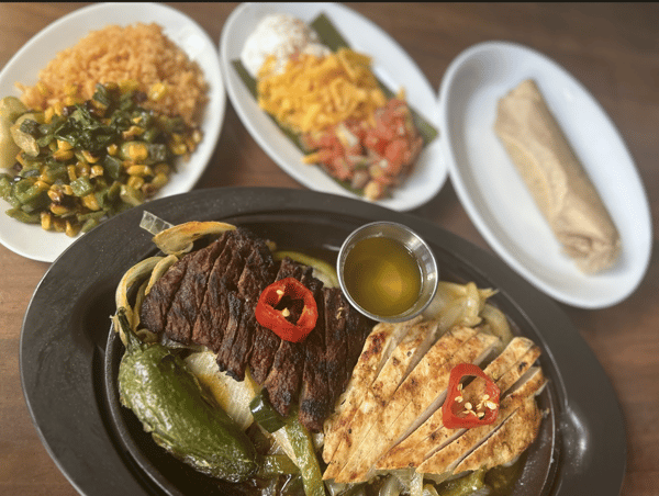 Mixed grill platter with steak and grilled chicken, sautéed peppers and onions, served with sides and tortillas