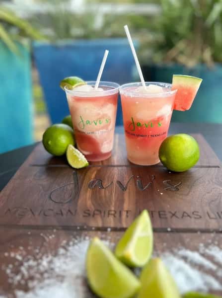Fresh watermelon margaritas with lime wedges on branded wooden board, vibrant Mexican cocktail presentation