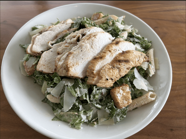 Grilled chicken Caesar salad with romaine lettuce, shaved parmesan, croutons, and creamy dressing on a wooden table