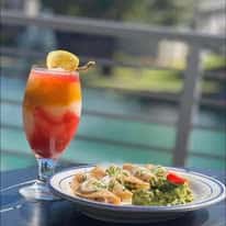 Tropical shrimp dish with cocktail featuring citrus garnish, outdoor waterfront dining setting