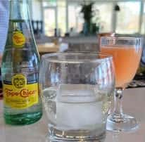 Bottled Topo Chico mineral water with iced water and citrus cocktail on restaurant table