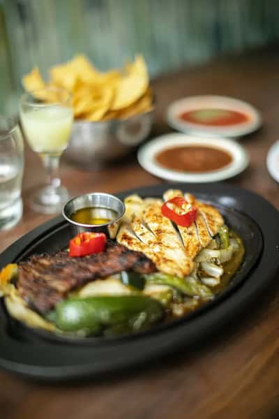 Sizzling steak and grilled chicken fajitas with peppers, onions, and dipping sauce, served with chips and salsa