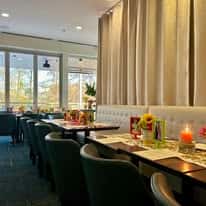 Modern restaurant dining room with upholstered seating, long table setup, candles, and natural light for an upscale ambiance
