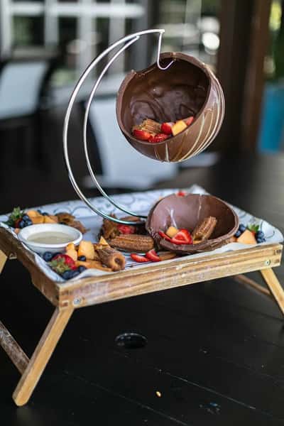 Chocolate dessert presentation with hanging chocolate shell, churros, fresh fruit, and dipping sauce, unique restaurant plating
