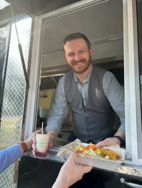 Friendly server handing tacos and a refreshing layered margarita through a food truck window, showcasing vibrant street food and casual dining experience
