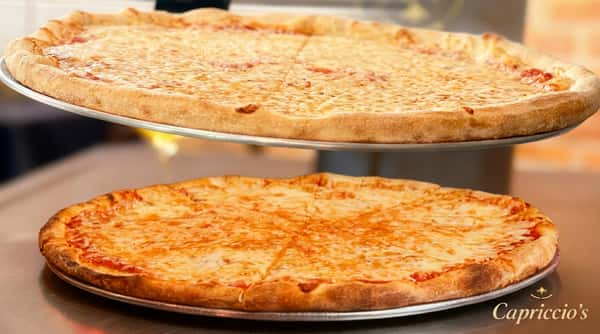 Two large, freshly baked cheese pizzas with golden-brown crusts stacked on metal trays.