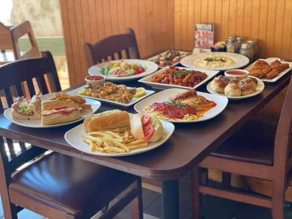 An assortment of Italian-American dishes including pasta, sandwiches, and appetizers spread across a wooden restaurant table.