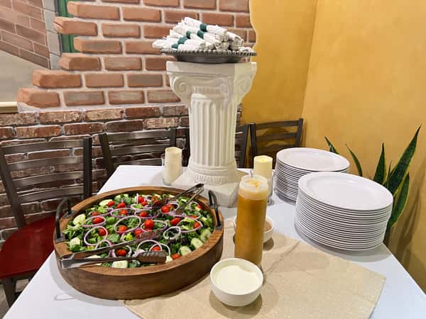Fresh garden salad in a large wooden bowl with stacks of white plates and dressings at a restaurant buffet station.