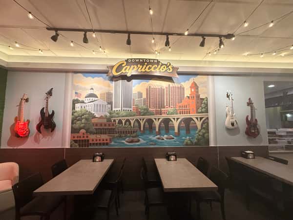 Modern dining area at Downtown Capriccio's featuring a large city mural, wall-mounted guitars, and dining tables under warm string lighting.