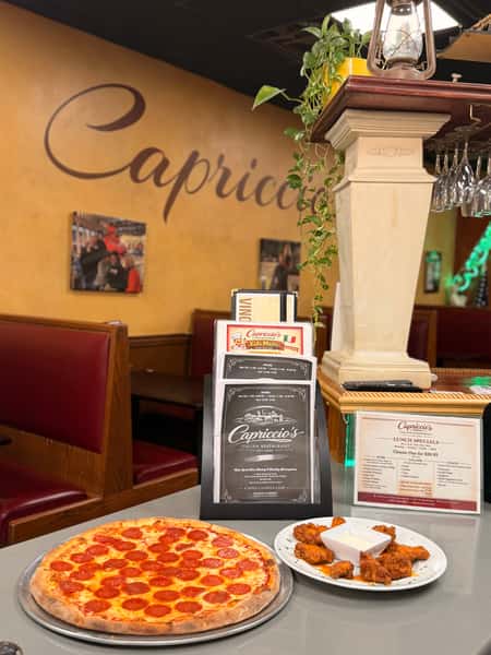 A pepperoni pizza and chicken wings on a restaurant counter with menus, red booths, and warm yellow walls in the background.