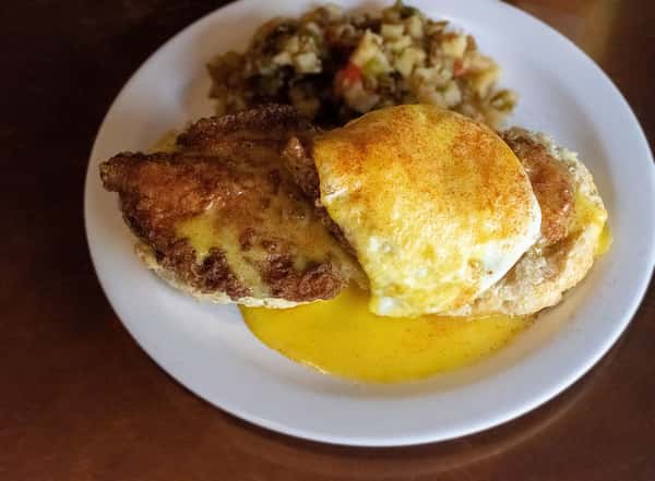 Open-faced biscuit with fried chicken, poached egg, and hollandaise, served with home fries.