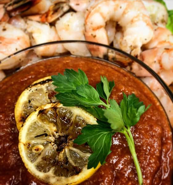 Chilled shrimp cocktail with cocktail sauce, grilled lemon, and fresh parsley.