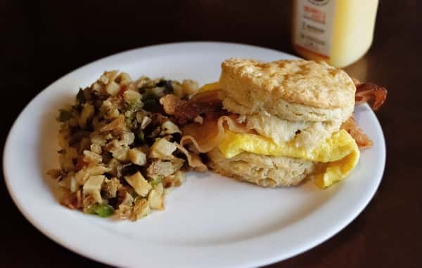 Bacon and egg biscuit sandwich served with sides.