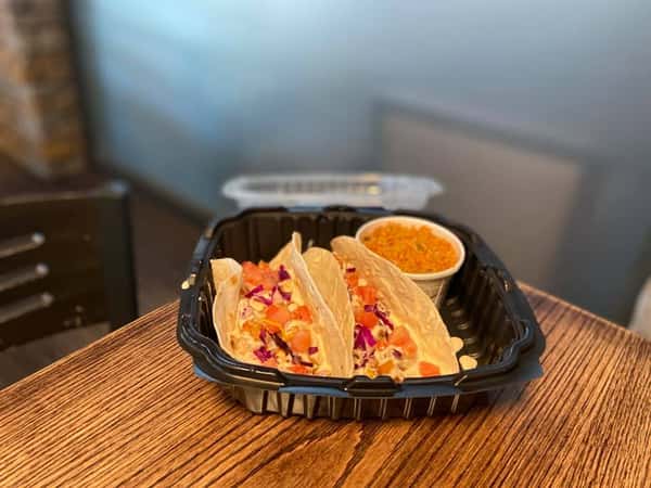 two tacos with dipping sauce in a to-go container