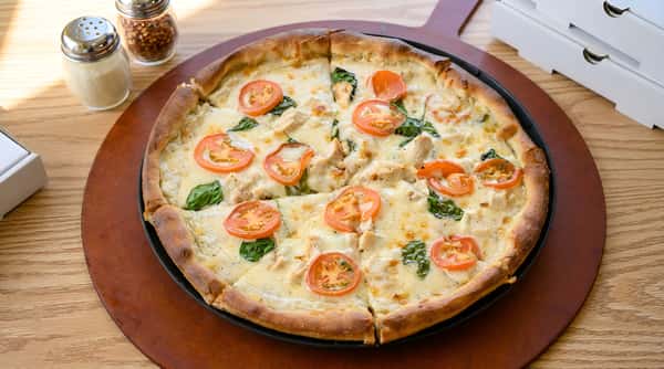 Chicken alfredo pizza with sliced tomatoes and spinach on a wooden board.