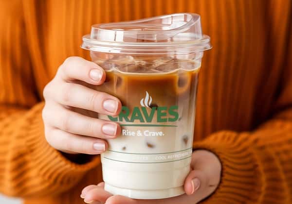 Person holding a plastic coffee cup with the logo branded on the side