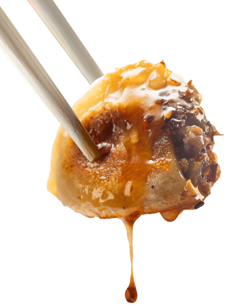 Chopsticks holding a dumpling dripping with sauce