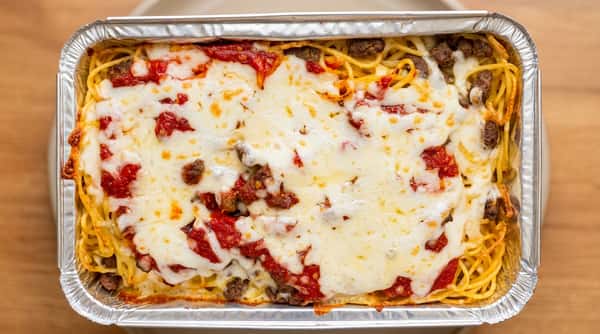 Baked spaghetti with melted cheese, marinara sauce, and ground meat in a foil tray.