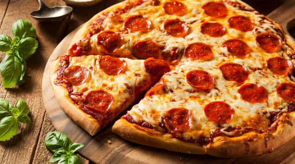 Pepperoni pizza with melted cheese and one slice removed, on a round wooden cutting board.