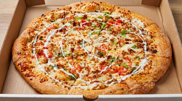 Large pizza with chicken, bell peppers, tomatoes, and a spiraling drizzle of white sauce in a cardboard box.