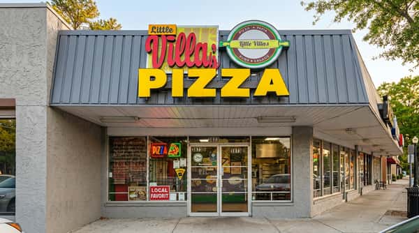 Little Villa's Pizza storefront sign with pink and yellow letters, and a green neon pizza sign in the window.