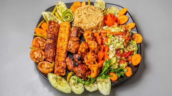 Large platter with grilled kabobs, rice, salad, sliced cucumbers, and carrots arranged around the edges.