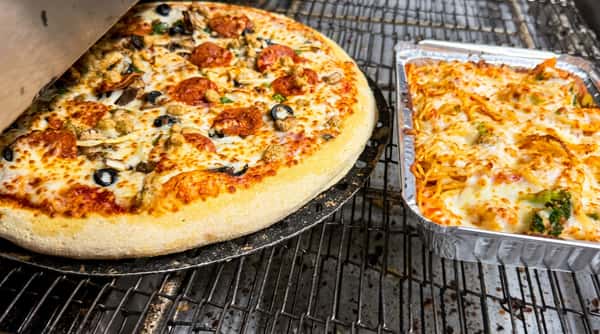 Pizza with pepperoni, mushrooms, and olives next to baked pasta with cheese and broccoli in a foil tray, on a metal rack.