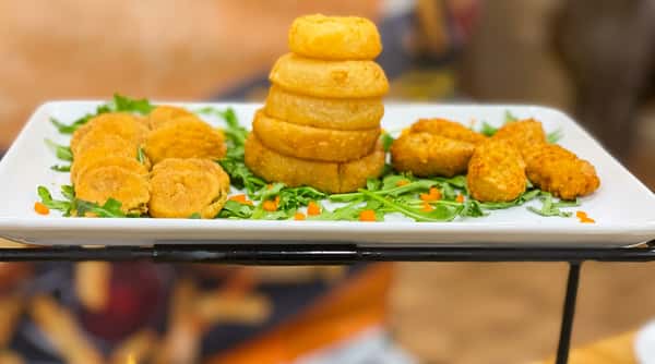 Fried onion rings stack and golden fried appetizers on a white platter with arugula and carrots.